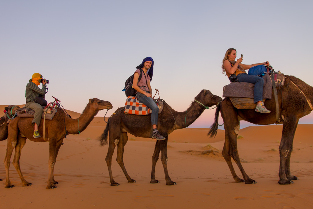 Three people riding camels in a desert in Morocco