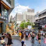 Bangkok’s Siam district with a colorful waving cat statue and people walking by