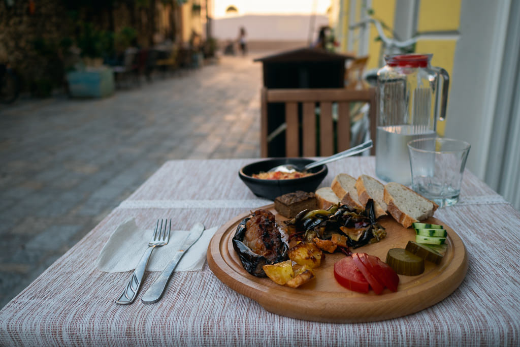Food, utensils, and a glass of drink on a table on a street in Albania.