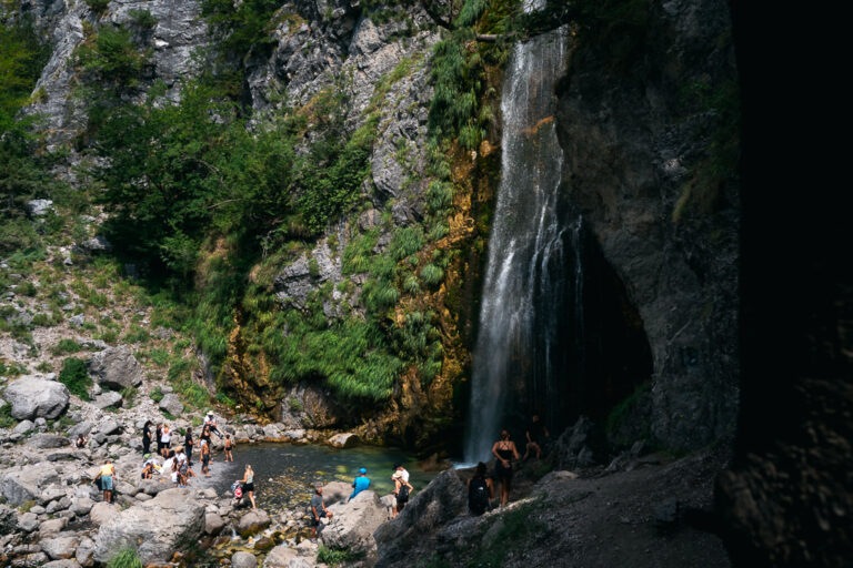 Grunas Waterfall in Theth National Park cascades down a mossy cliff with people around it