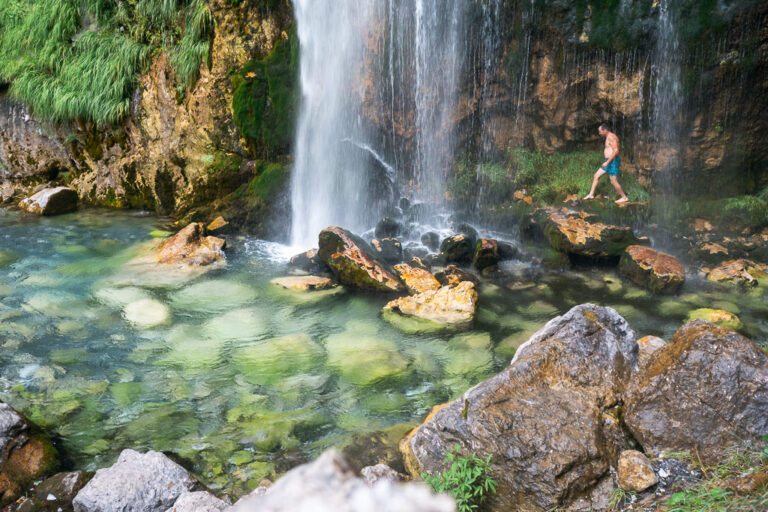 Man walks on rocks at the base of a waterfall in the Albanian Alps