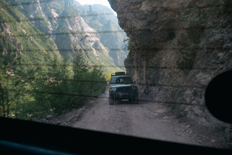 View from a vehicle of an SUV on a dirt road along a cliff in the Albanian Alps
