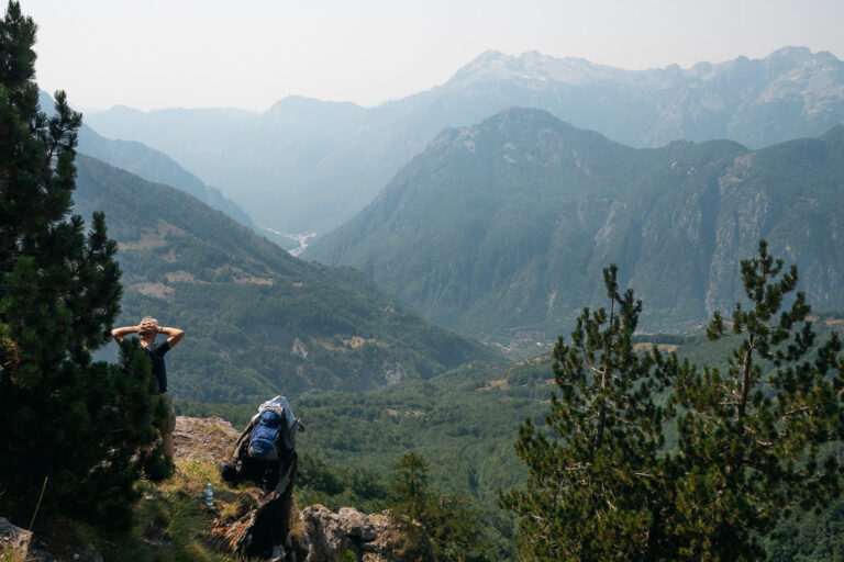 view of the Albanian Alps with a hiker overlooking a misty, forested valley