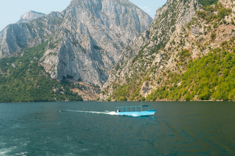 Komani Lake in Albania, with steep green mountains and a small boat gliding between the cliffs