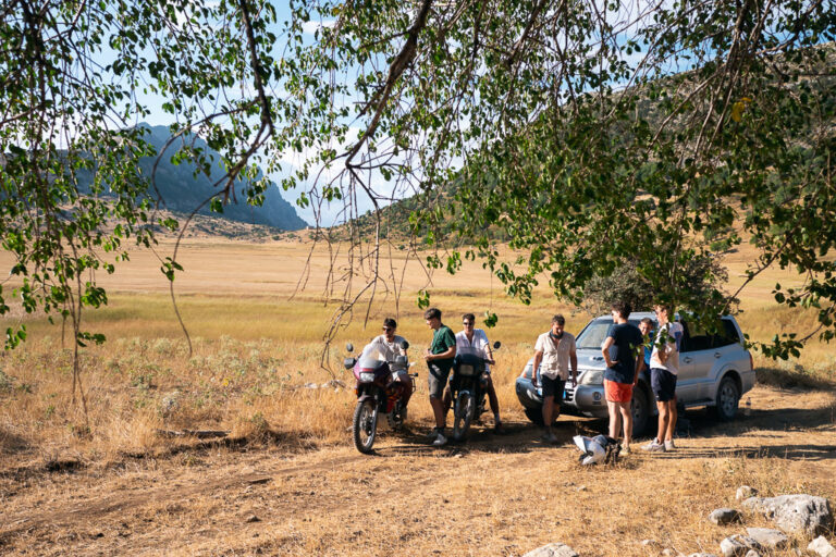 Group of friends with a car and bikes under a tree in a mountain meadow of the Albanian Alps