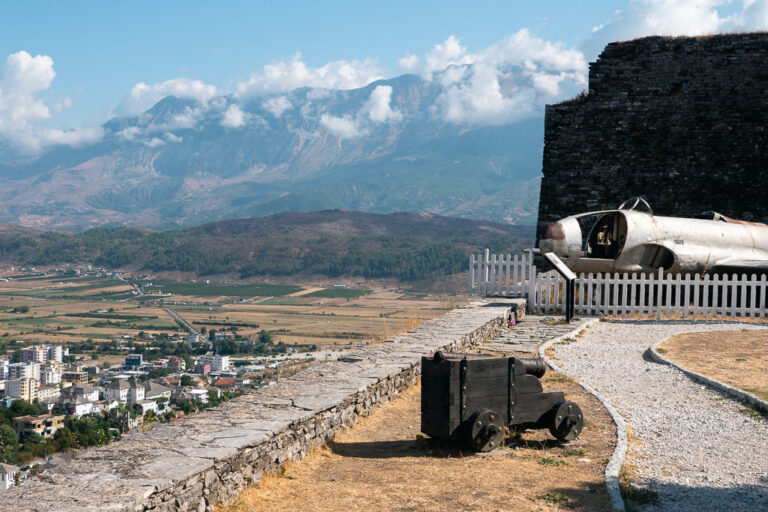 The outside of a museum in Gjirokaster, Albania with canyon, old aircraft, and a view of the city below and the mountains.
