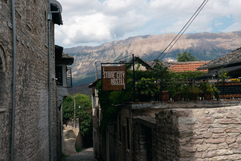 Steep cobblestone street in Gjirokaster showing Stone City Hostel and mountains in the background