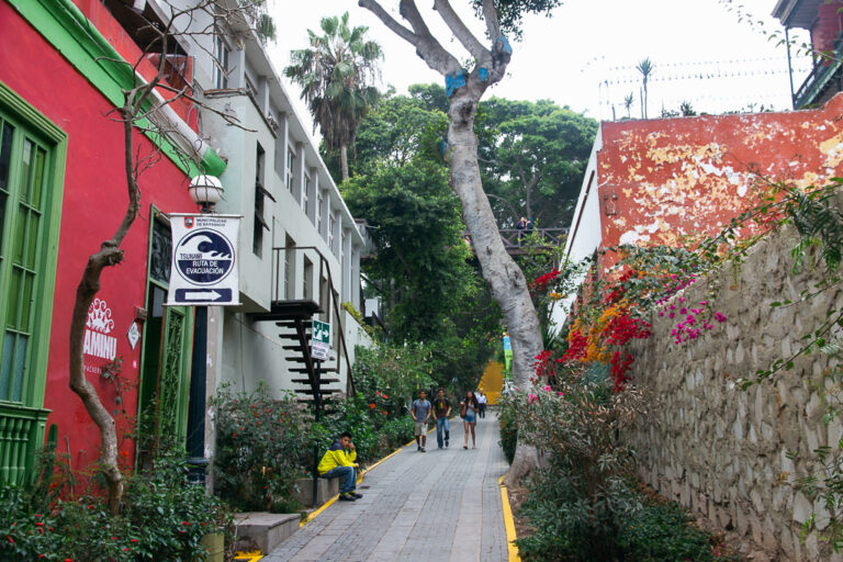 Colorful pedestrian street in Barranco, Lima, with bright walls, flowers, and people walking toward the Bridge of Sighs