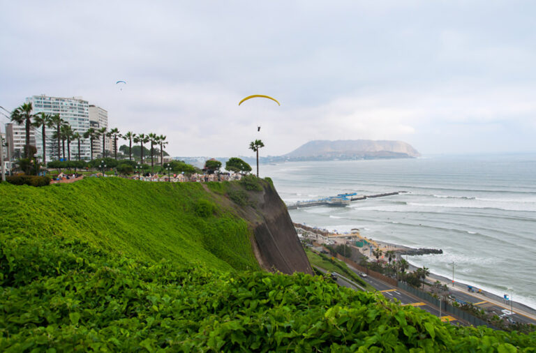 Lima’s Costa Verde showing green cliffs, coastal highway, and two paragliders over the ocean