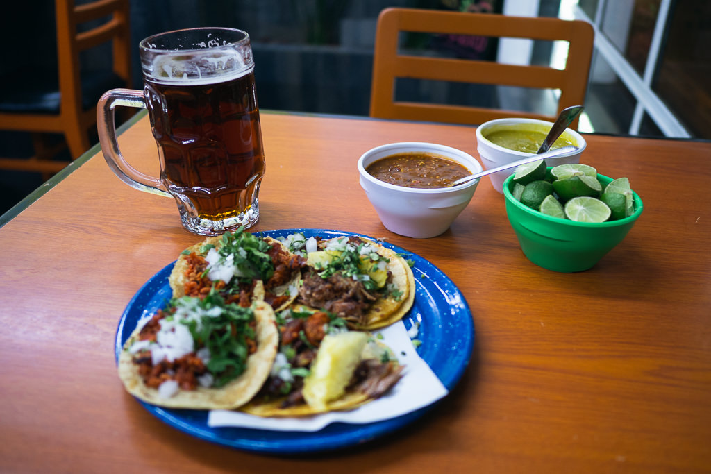 A table with a plate of tacos, drink, and condiments