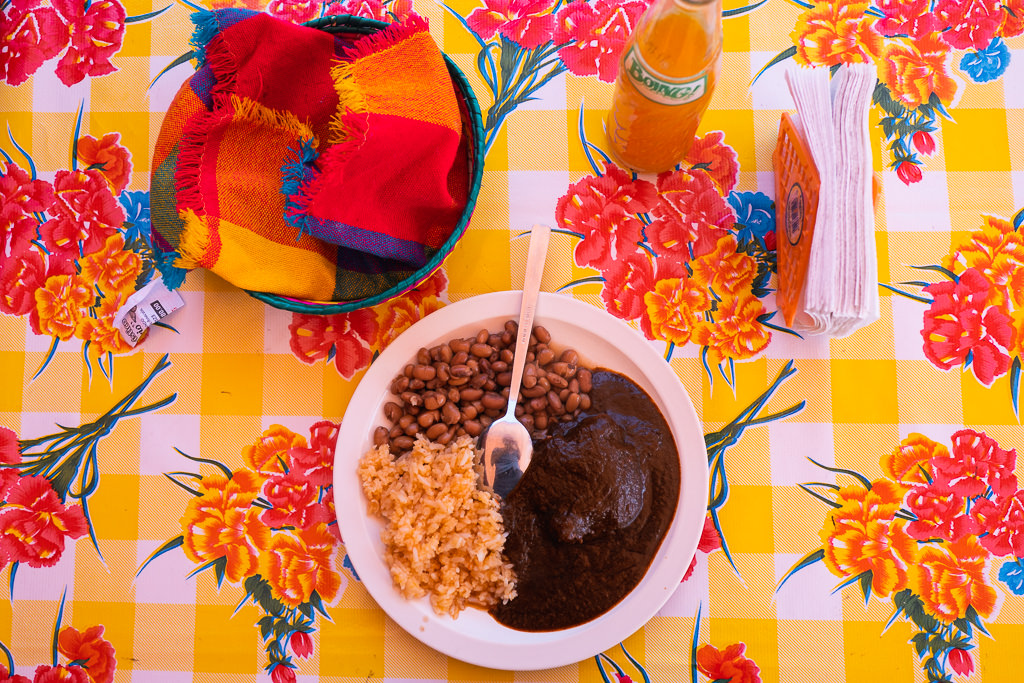 A plate of beans and other food, a bottle of drink, and tissues on a table with floral print. 