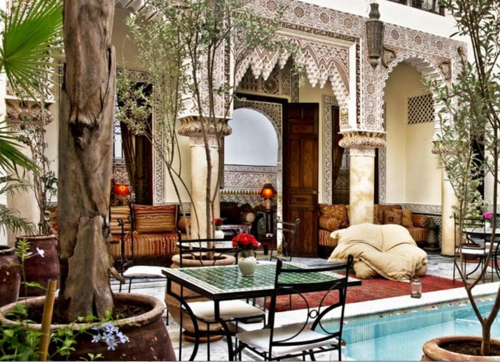 An outdoor center with a pool, surrounded by plants and furniture, in a riad in Marrakech
