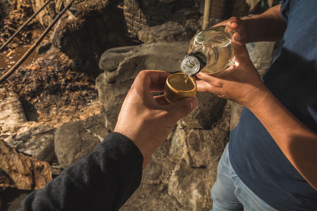 A man pouring mezcal into a shot glass held by another person