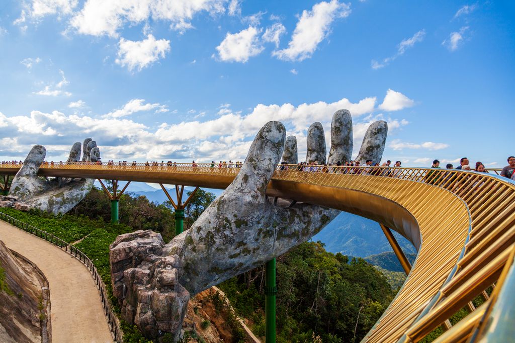 Tourists on Vietnam's Ba Na Hills Golden Bridge being supported by a giant sculpture hand