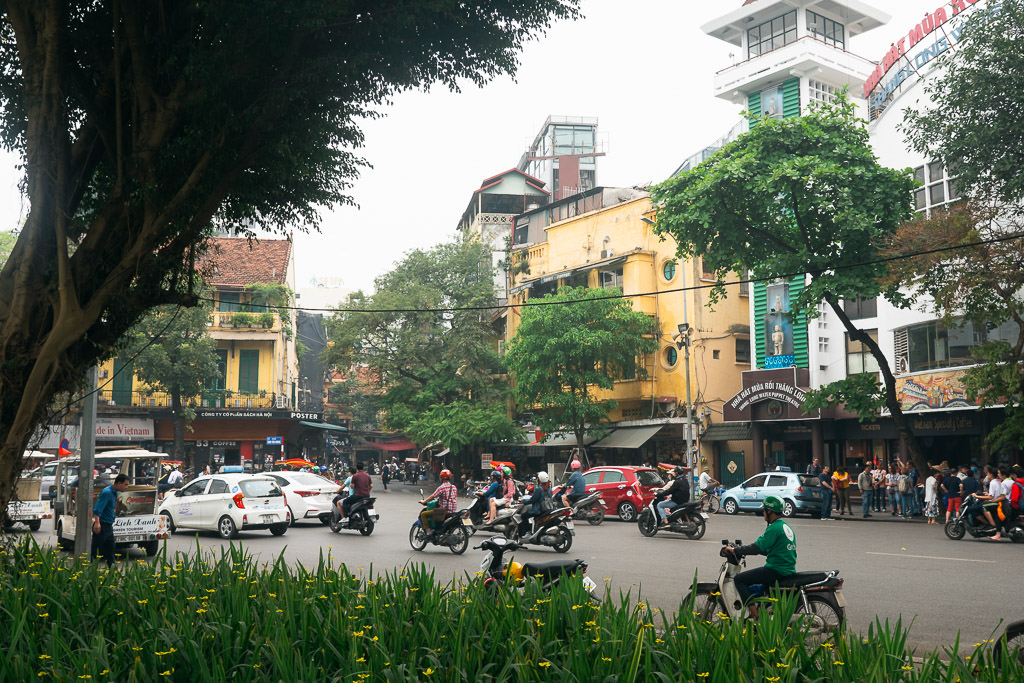 daytime shot of a busy Hanoi street with traffic, motorbikes, and pedestrians