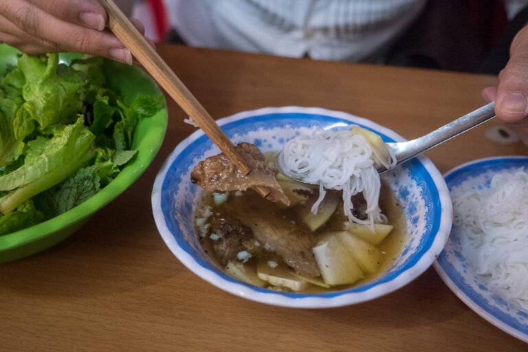 a bowl of Bún chả, showing a person using chopsticks to eat