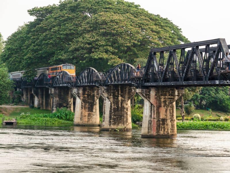 A train approaching on a bridge over a river in Thailand.