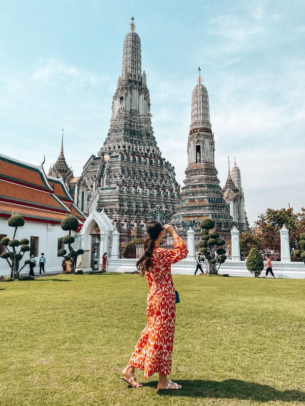 A woman standing outdoors in front of Wat Arun temple in Bangkok, Thailand.