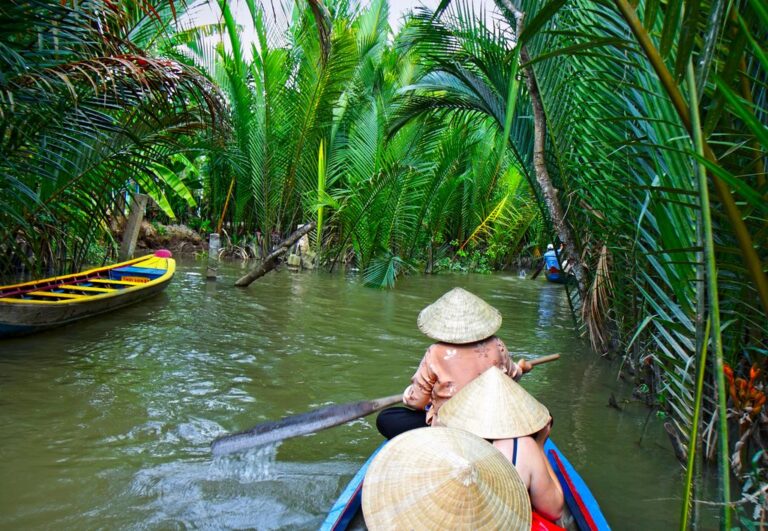 People wearing hats riding a boat through a canal in Mekong Delta, Vietnam.
