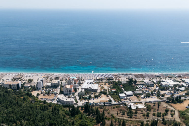 Areal view of a sunny beach area in Dhërmi with a cluster of buildings and greenery 