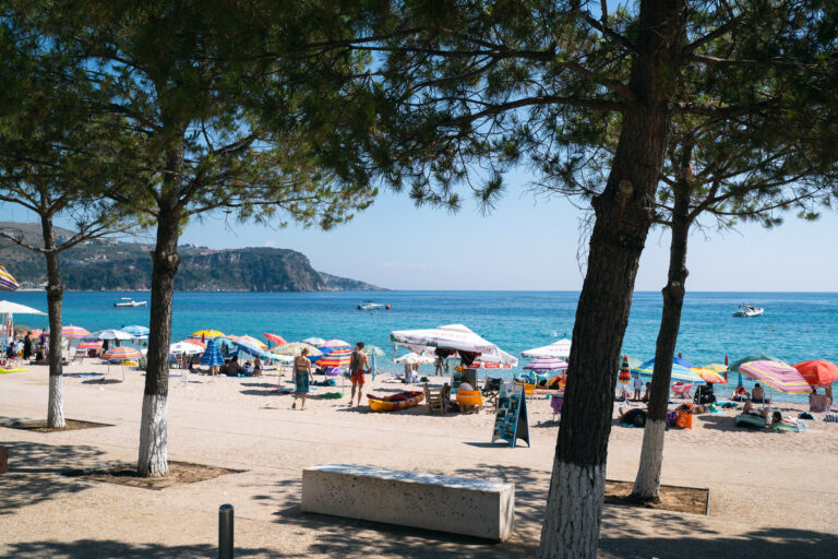 A sunny view of a beach in Himarë, Albania, framed by green trees