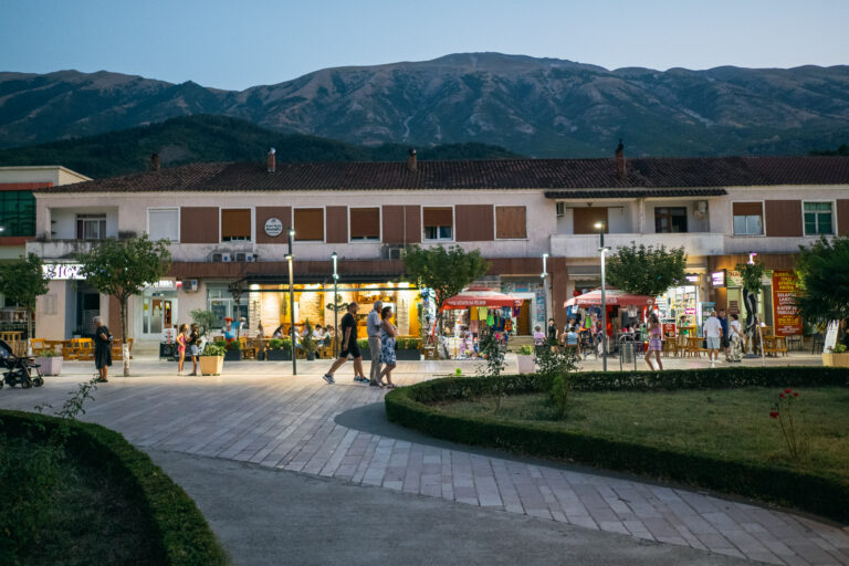 Evening view of Permet’s town square with lit-up cafes and shops