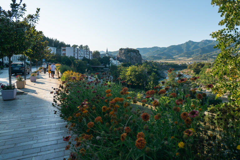 Sunny pedestrian walkway in Permet's city park lined with wildflowers