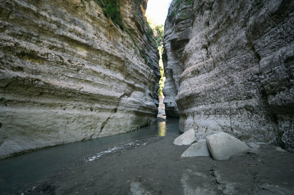 narrow slot in Langarica Canyon with towering walls and a shallow stream below