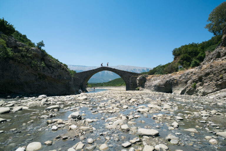 People walking over the Kadiut Bridge crossing a rocky riverbed in Langarica Canyon