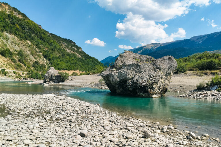 View of the Vjosa River in Albania, flowing around large boulders across a stonebed