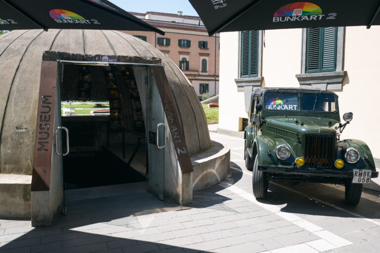 The entrance of Bunk'art 2 with a concrete, dome-shaped bunker structure and a vintage, dark green military jeep
