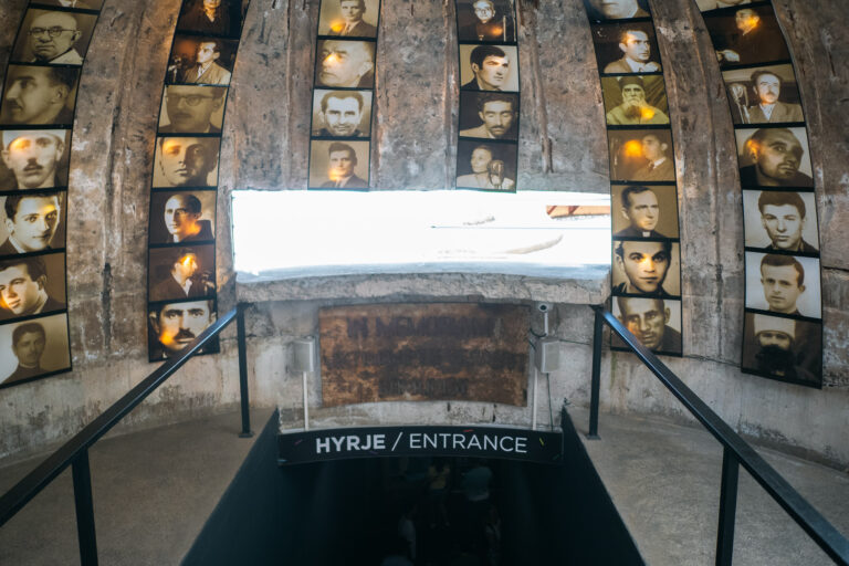 Bunk’Art 2 entrance with walls lined with backlit square portraits and a dark staircase leading deeper inside