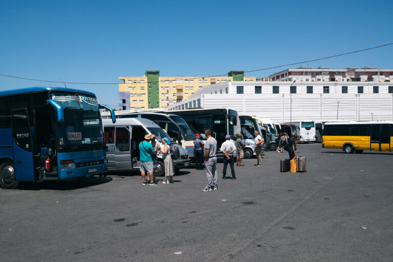 A bus station in Tirana with buses queued and travelers milling about