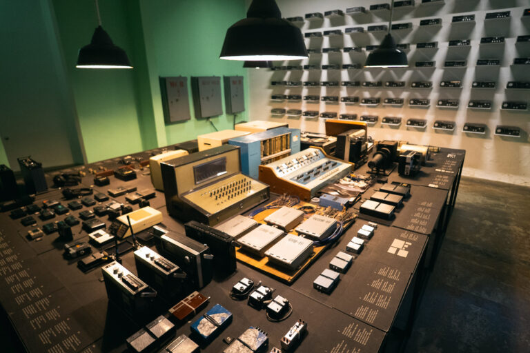 A central square table holds vintage surveillance devices arranged in a grid in the House of Leaves