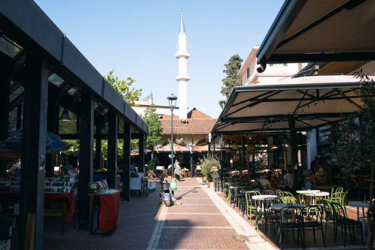Street view of Tirana’s New Bazaar with brick walkway, open-air cafe, and market stalls