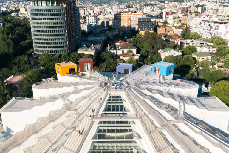 Aerial view of the Pyramid of Tirana with colorful rooftop boxes and Tirana skyline in the background