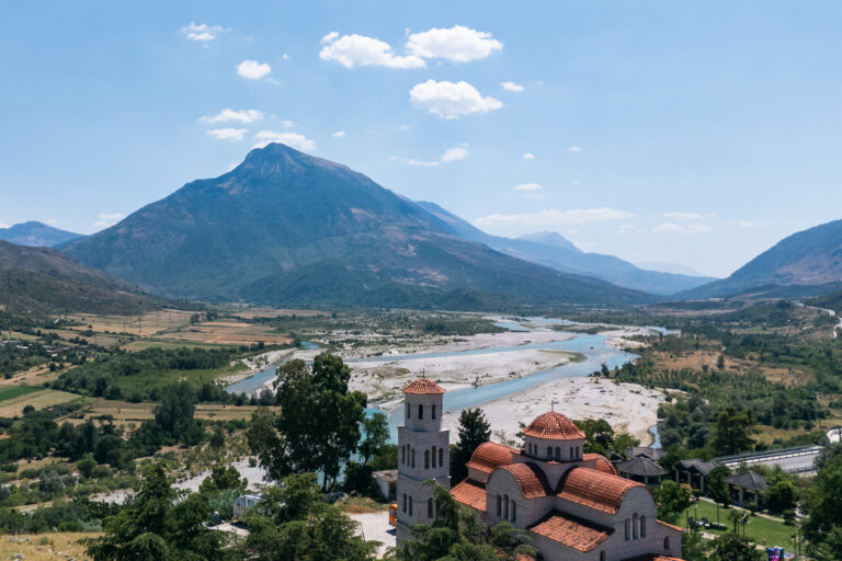 View of a small Orthodox church by the Vjosa River with a steep mountain rising in the background located near Tepelena