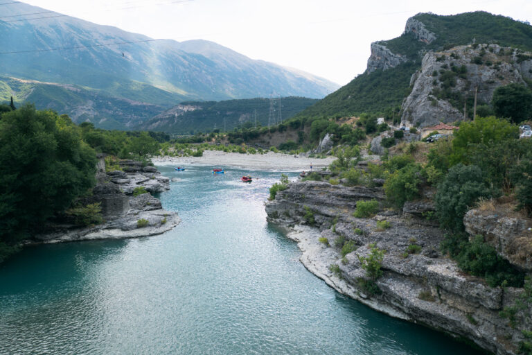 Vjosa River winding past boulders with forested slopes and mountains in the background