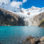 man swims in Laguna Parón with towering snow-capped mountains and a massive glacier in the background