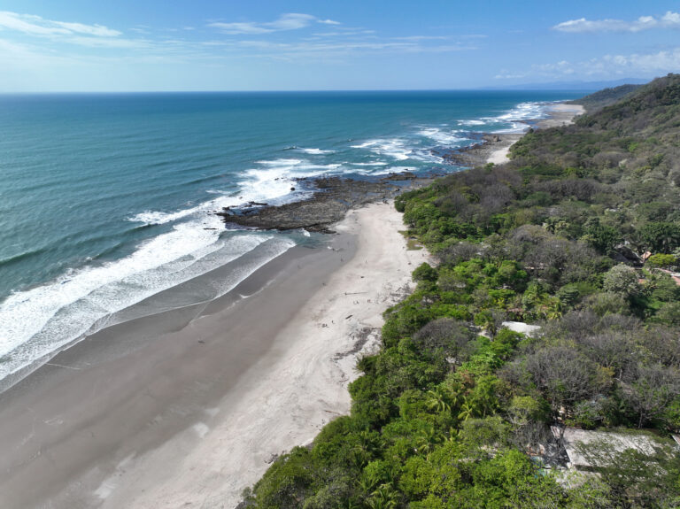 An aerial view of the Santa Teresa coastline in Costa Rica, showing a long sandy beach alongside lush forests