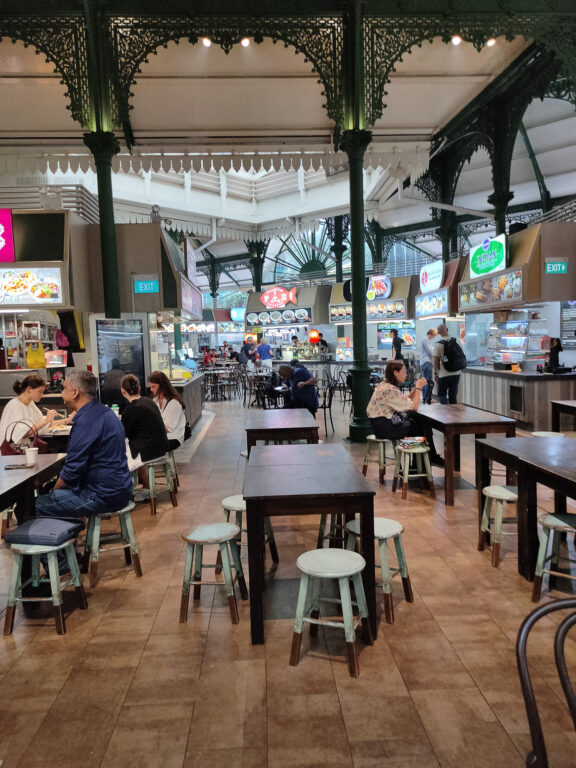 Interior of a crowded hawker centre with high ceilings and people seated at dinner tables