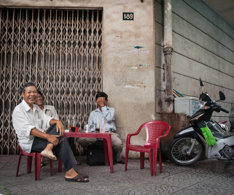 Three older men sitting at a low table on a sidewalk outside a building in Ho Chi Minh Cit