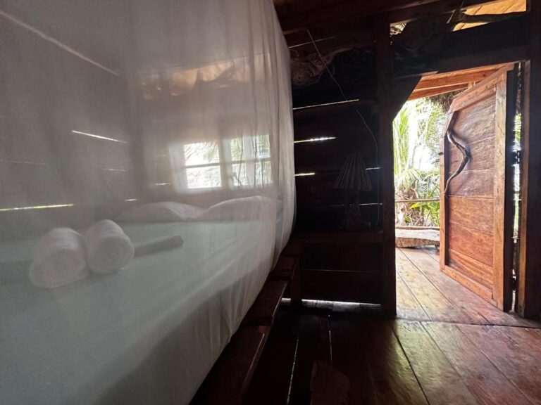 A wooden bedroom in Ensuenos Natural Suites with a white mosquito net over the bed and an open rustic door