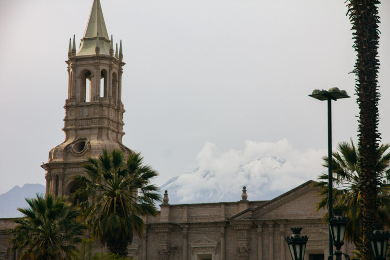 Cathedral bell tower in Arequipa with a snow-capped volcano and palm trees