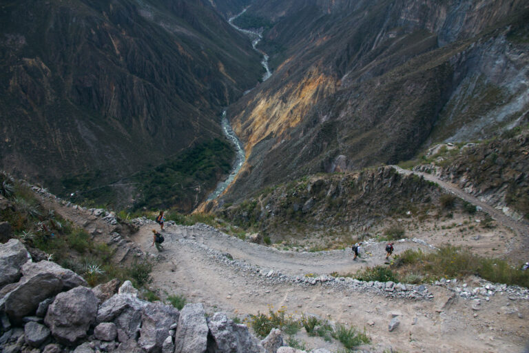Hikers descending a winding dirt path into Colca Canyon