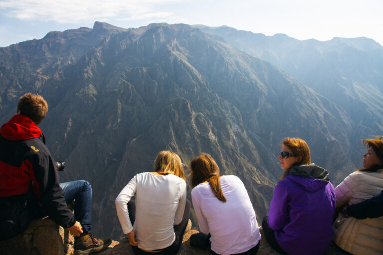 Hikers sitting on a ledge overlooking the vast landscape of Colca Canyon
