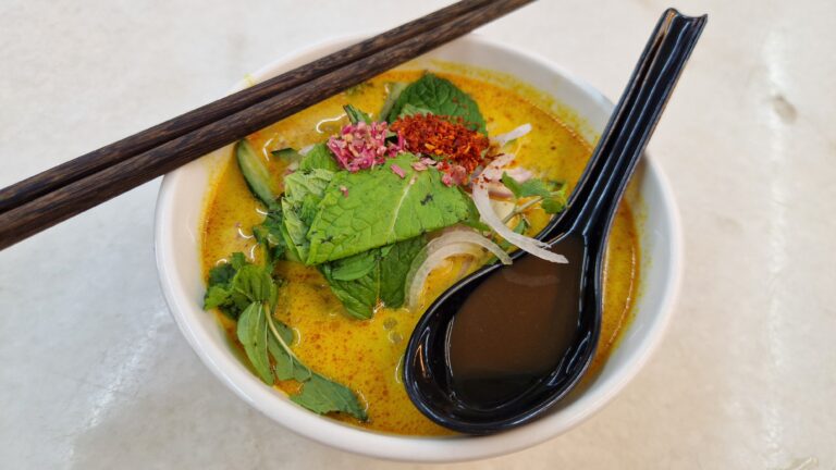 Bowl of Penang lemak laksa with creamy broth, herbs, and chopsticks