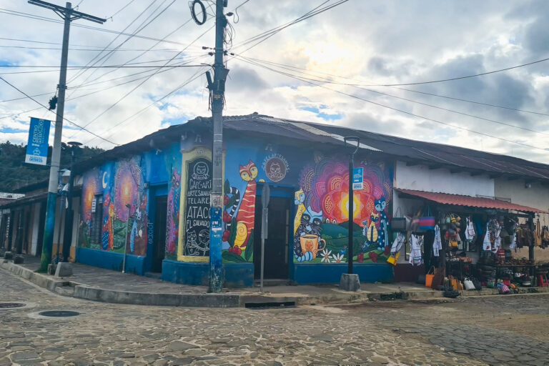 A blue corner building in Ataco covered in colorful murals of cats and floral patterns 