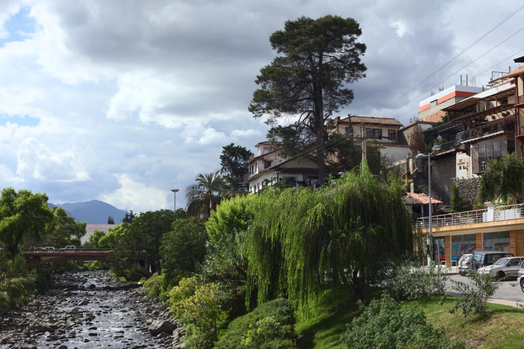 the Tomebamba River flowing through Cuenca, Ecuador, with historic buildings and lush greenery along the banks
